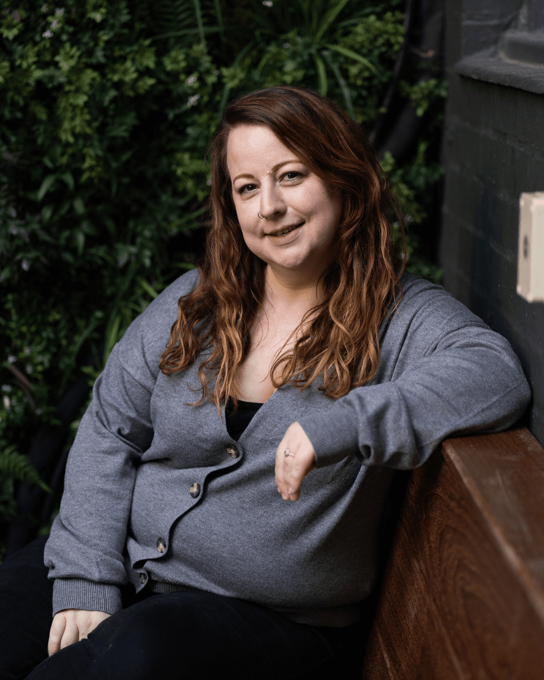 image of the owner, Lianne Harris sitting down smiling. She has red wavy hair and a grey cardigan on.